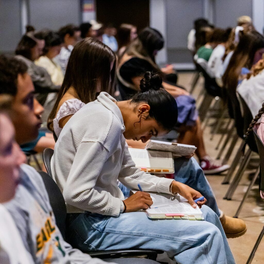 Students attentively taking notes during a classroom lecture setting indoors.