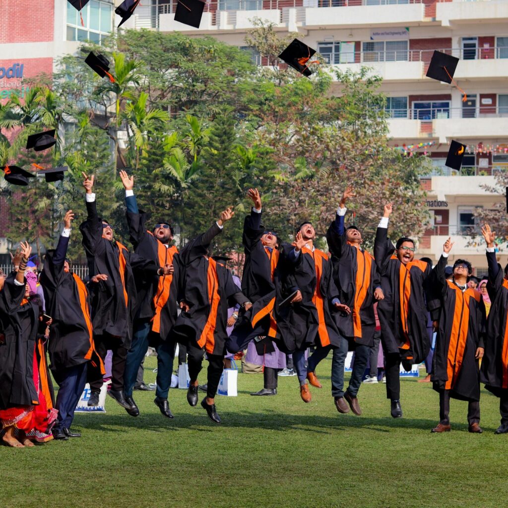 Graduates joyfully toss caps in the air during outdoor ceremony, celebrating graduation day.
