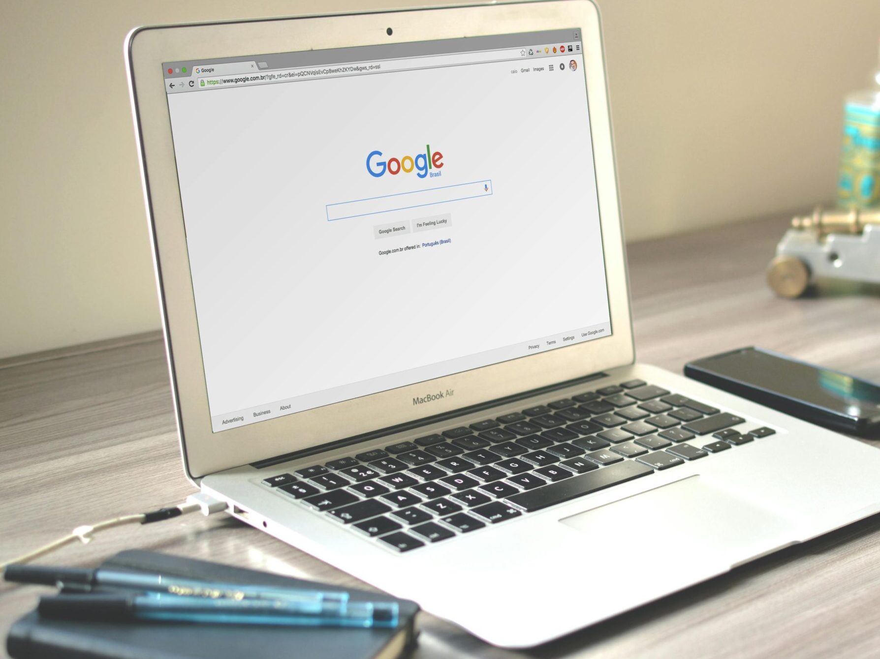 A neat workspace featuring a laptop displaying Google search, a smartphone, and a notebook on a wooden desk.
