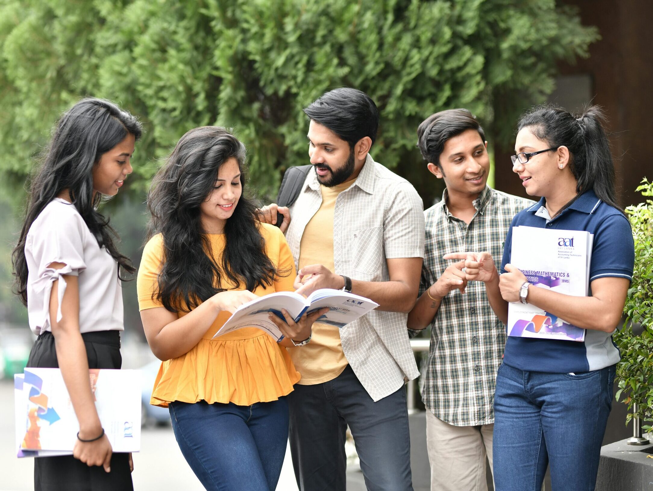 A group of diverse college students engaged in outdoor group study session, sharing books and ideas.