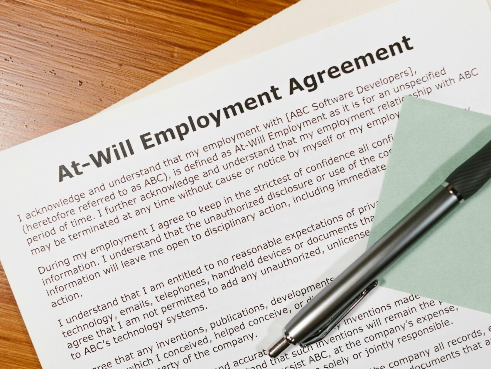 Close-up of an at-will employment agreement on a wooden desk with a pen, emphasizing legal and business concepts.