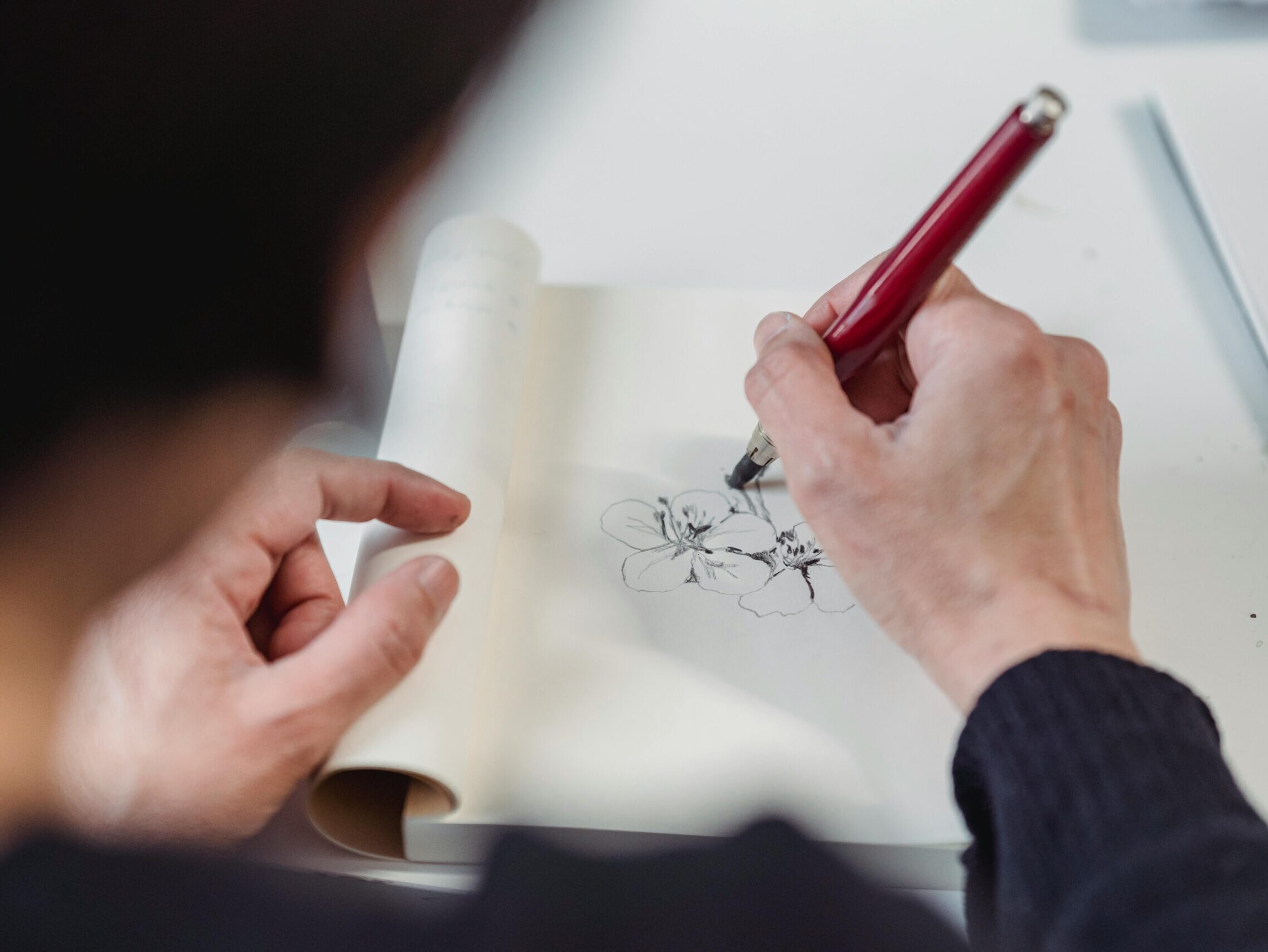 Close-up of a hand drawing floral sketch with a pen, emphasizing creativity and artistic expression.